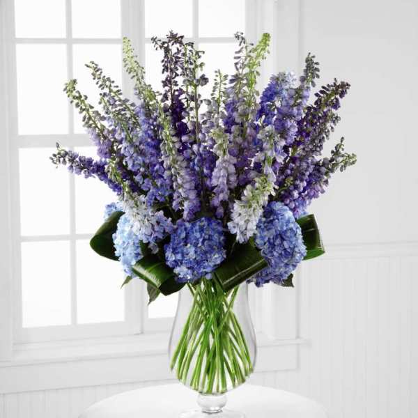 Tall blue and purple floral arrangement in a clear glass vase