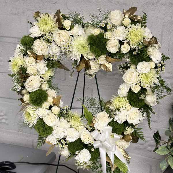 Heart-shaped white floral wreath on an easel with a ribbon bow