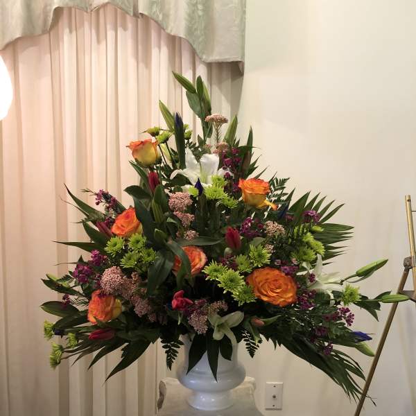 Large floral arrangement with orange roses in a white vase