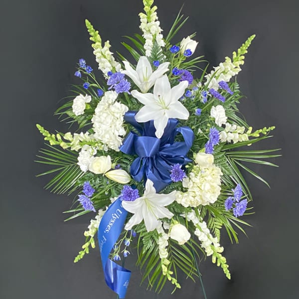 White lilies and blue flowers in a funeral spray with a blue ribbon