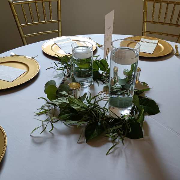 Round table with gold chargers and greenery centerpiece around glass candles