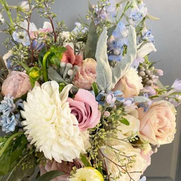 Pastel bouquet with white dahlia, blush roses, and light blue flowers against a gray background