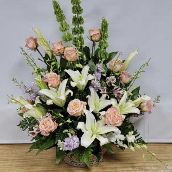 Large floral arrangement with white lilies, peach roses, and purple accents in a basket