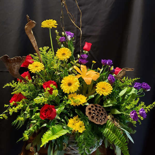 Large mixed floral arrangement with red roses, yellow daisies, and purple blooms