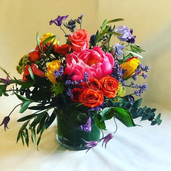 Mixed bouquet of roses, peonies, and purple flowers in a glass vase