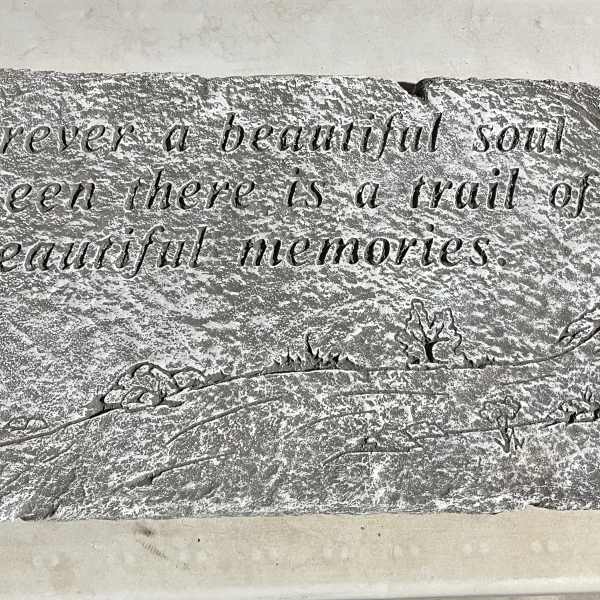 Rectangular gray memorial stone engraved with a sentimental quote and small landscape motifs.