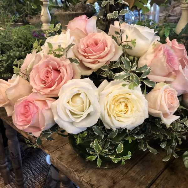 Low arrangement of pink and white roses with variegated foliage in a glass bowl vase