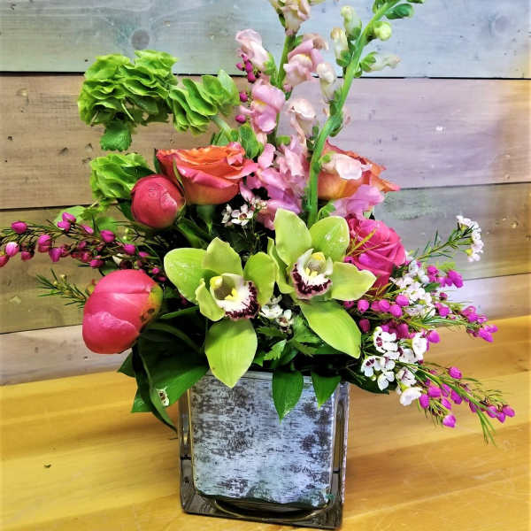 Mixed floral arrangement in a square glass vase with pink and green blooms