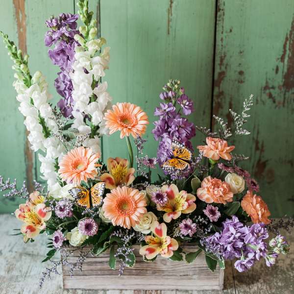 Mixed floral arrangement in a wooden box with peach, purple, and white blooms