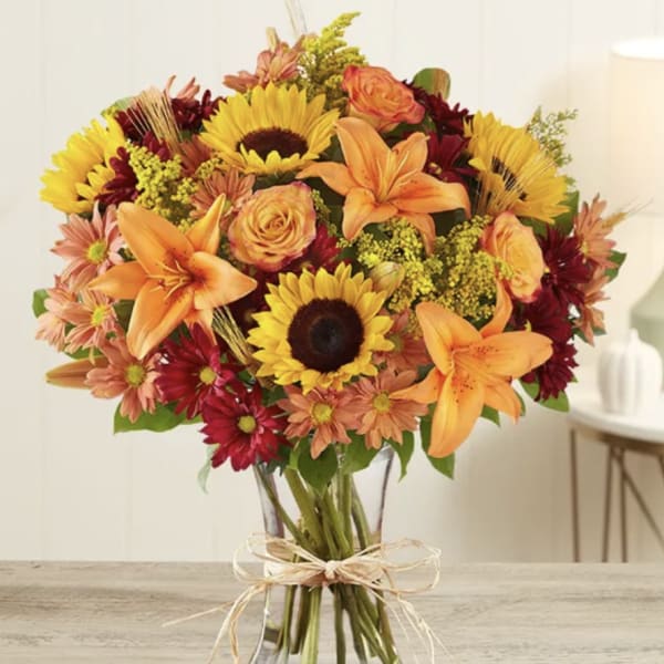 Bouquet of sunflowers, orange lilies, and roses in a glass vase