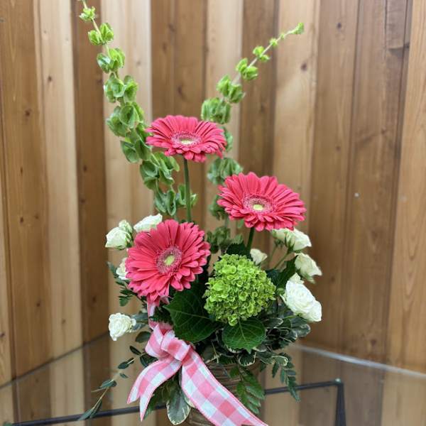 Everyday arrangement with pink gerbera daisies, green hydrangea, and white blooms in a glass vase with a pink bow.