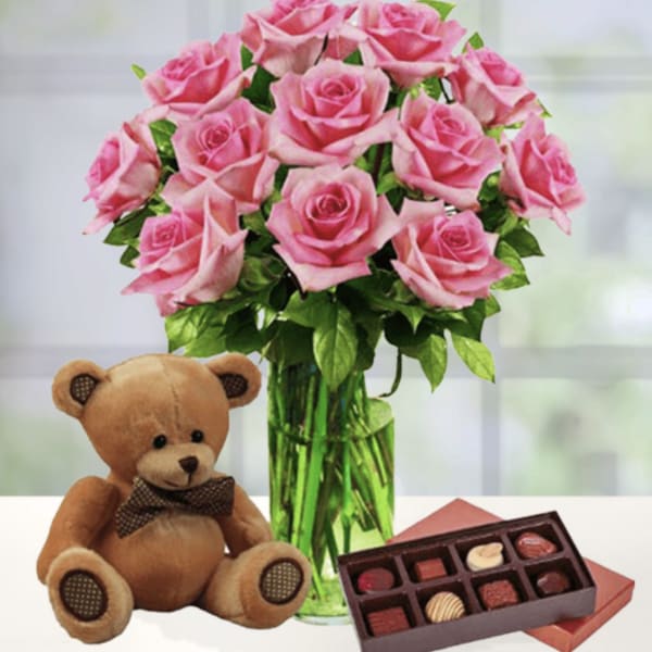 Pink roses in a glass vase with a teddy bear and chocolates