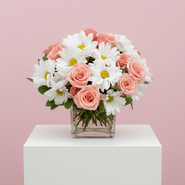 Arrangement of peach-pink roses and white daisies in a square glass vase on a white pedestal.