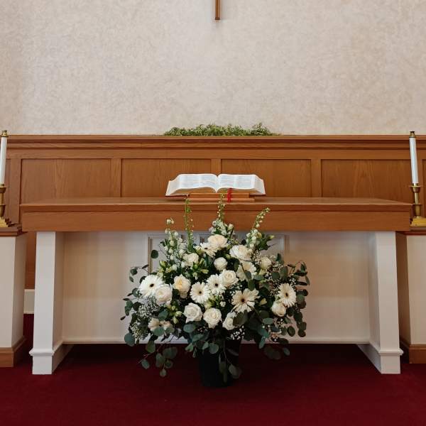 White floral arrangement beneath a church altar with a cross above
