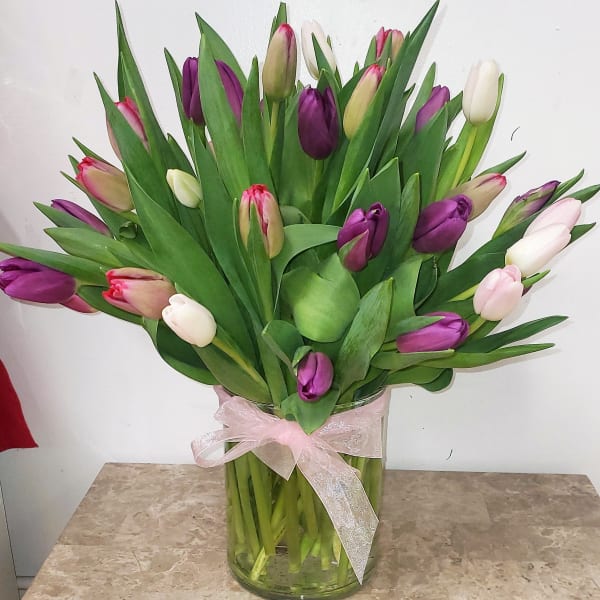 Bouquet of purple, pink, and white tulips in a glass vase with a pink ribbon