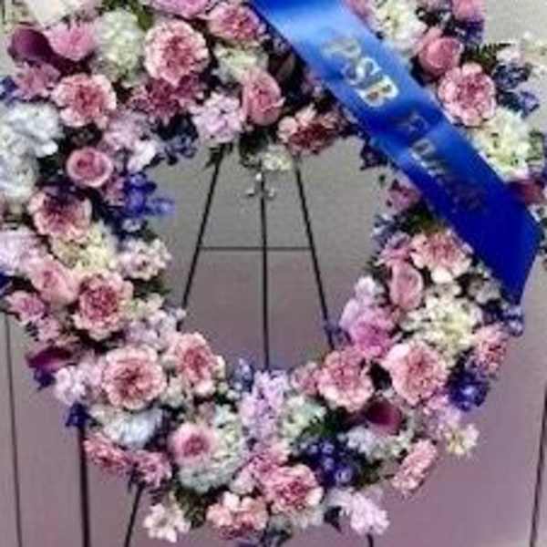 Large floral wreath of pink, white, and purple flowers on a stand with a blue ribbon