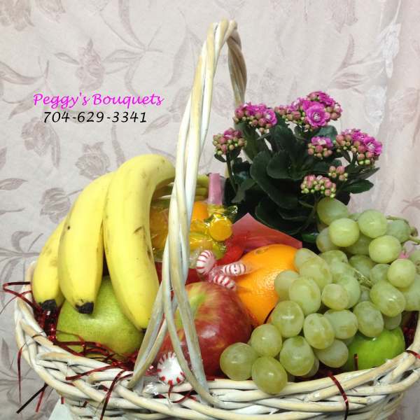 Fruit basket with bananas, grapes, oranges, apples, and a potted pink flowering plant
