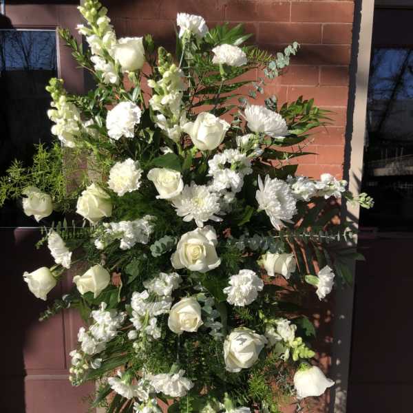 Tall standing spray of white roses, carnations, and other flowers on a metal easel