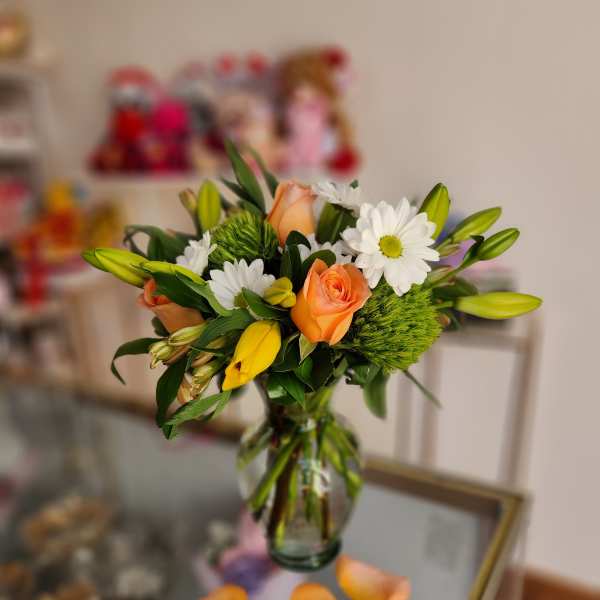 Bouquet of orange roses, white daisies, and yellow lilies in a glass vase