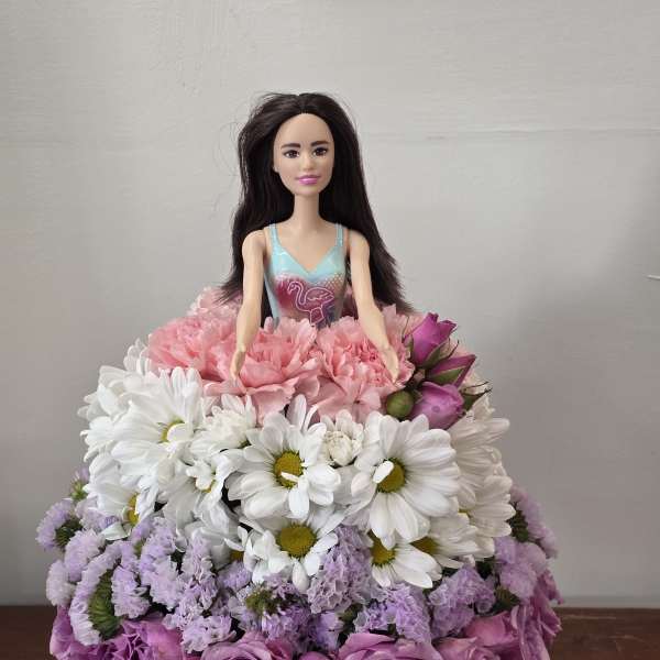 Doll in a dress surrounded by a pink, white, and purple flower arrangement