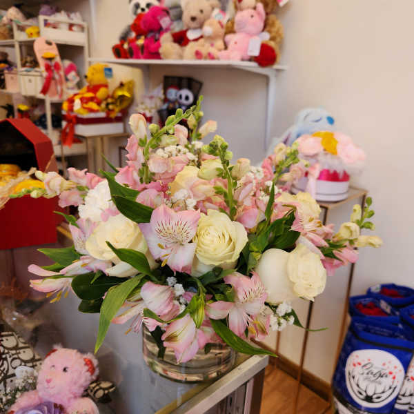 Round arrangement of white roses and pink alstroemeria in a clear glass vase on a shop counter.