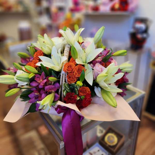 Bouquet of white lilies, orange roses, and purple orchids wrapped with ribbon