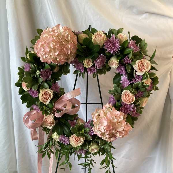 Heart-shaped floral wreath with pink hydrangeas, roses, and purple blooms on a stand