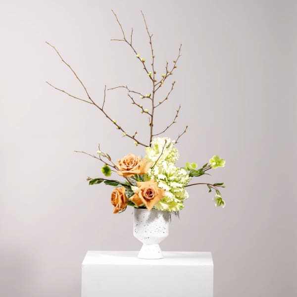 Peach roses and white-green flowers in a white vase with bare branches