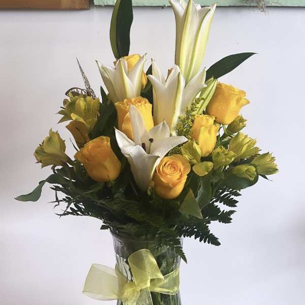 Yellow roses and white lilies in a clear glass vase with a ribbon