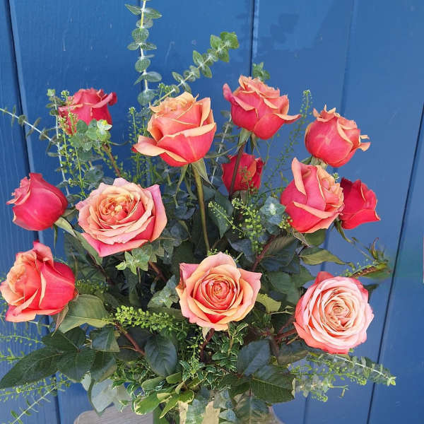 Tall arrangement of coral and orange roses in a clear glass vase on a small wooden table