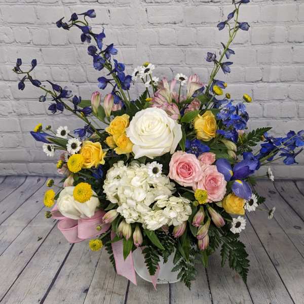 Mixed bouquet with roses, hydrangea, and blue delphinium in a white container