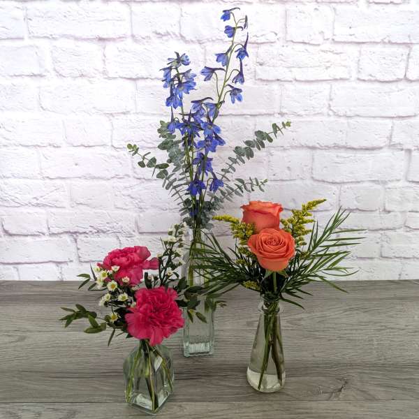Three small flower arrangements in glass vases with blue, pink, and orange blooms