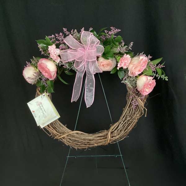 Pink rose wreath with a large ribbon bow on a grapevine frame