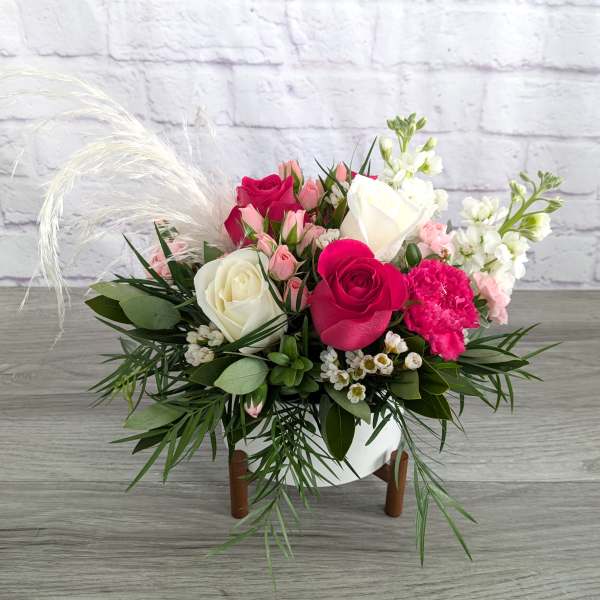 Pink and white rose bouquet in a white vase with feathery accents