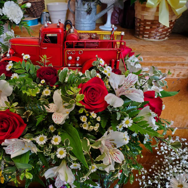 Red roses and white lilies arranged around a red toy truck