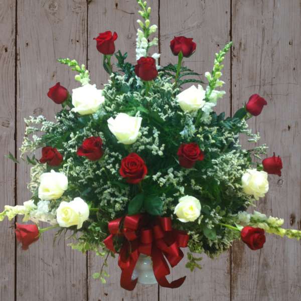 Red and white roses arranged in a vase with a red ribbon