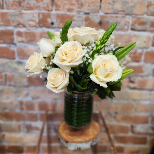 Cream roses arranged in a glass vase with green accents