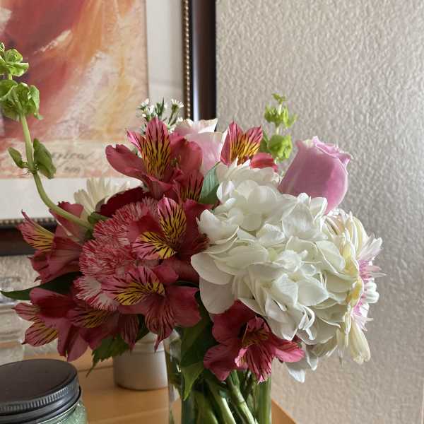 Mixed bouquet of pink alstroemeria, white hydrangeas, and a pink rose in a clear glass vase on a table