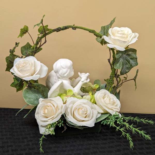 White roses arranged around a small angel figurine in a decorative container