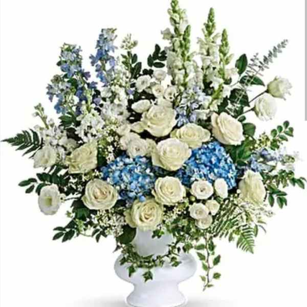 White roses and blue flowers arranged in a white pedestal vase