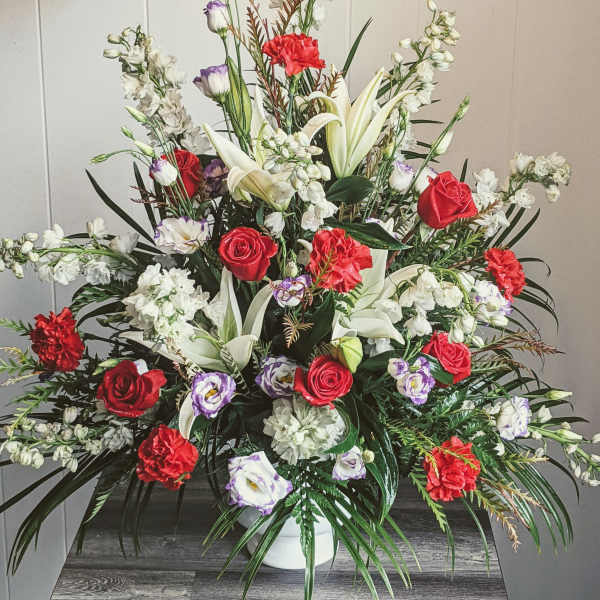 Large mixed floral arrangement with red roses, white lilies, and white blossoms in a vase