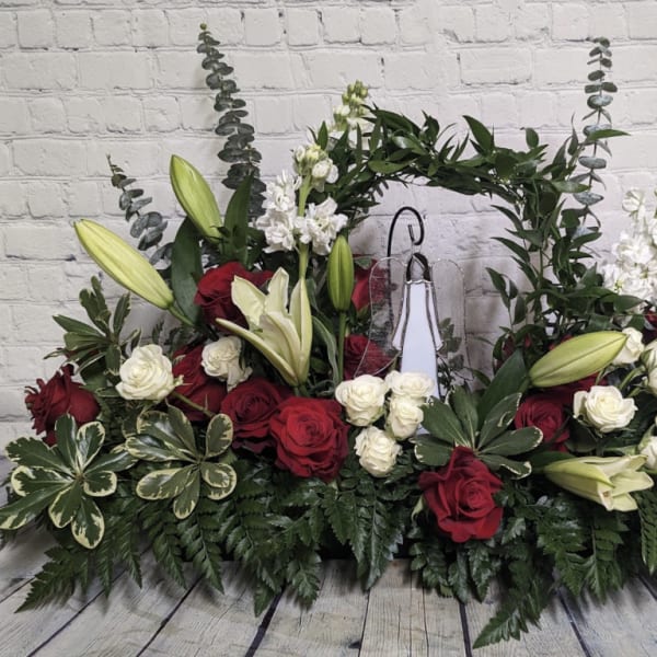 Symmetrical floral arrangement with red and white roses, lilies, and greenery around a central cross
