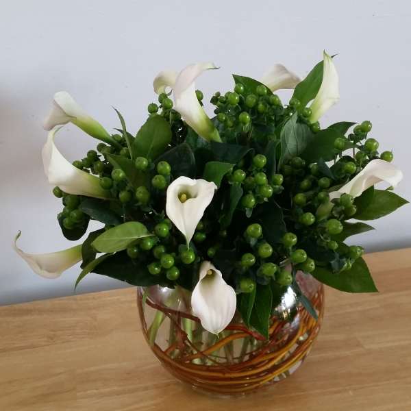 White calla lilies in a glass vase with green berry clusters