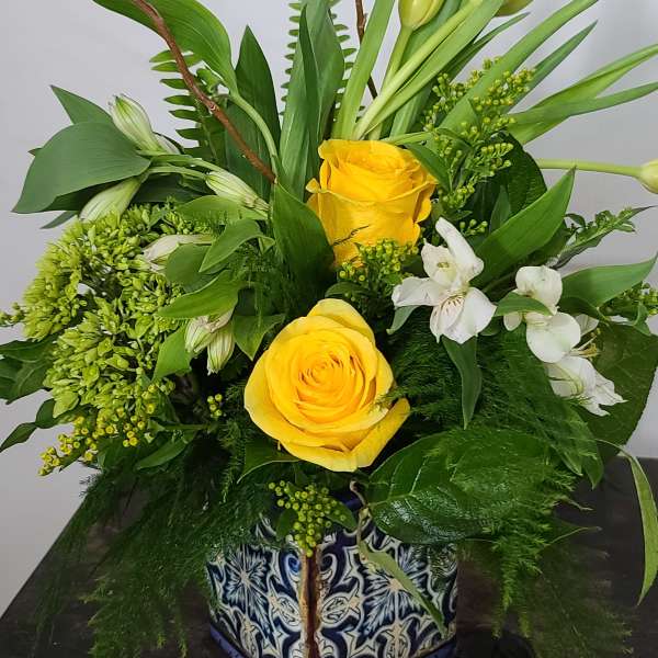 Yellow roses and white flowers in a patterned square vase