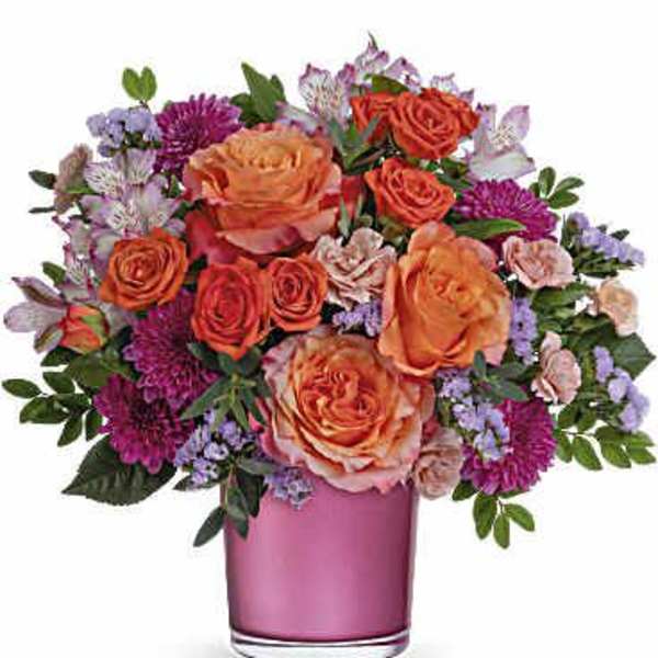 Orange and pink mixed flower bouquet in a pink glass vase