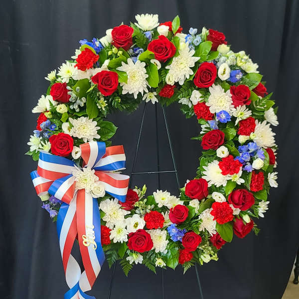 Circular wreath of red, white, and blue flowers with a ribbon bow
