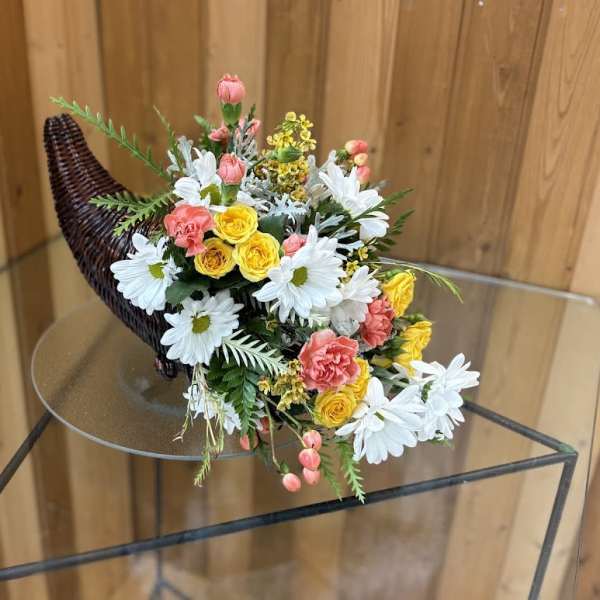 Bouquet of white daisies, yellow roses, and pink flowers in a wicker horn-shaped holder
