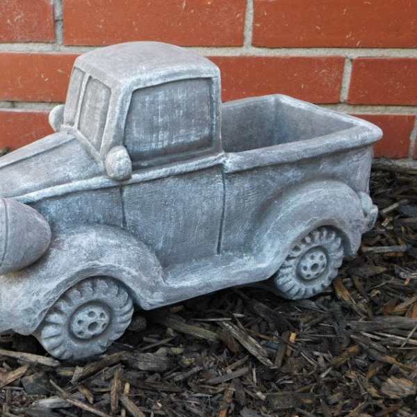 Gray pickup truck-shaped planter on mulch in front of a brick wall