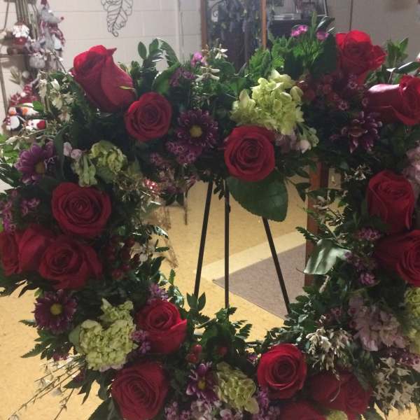 Heart-shaped floral wreath with red roses and purple flowers on an easel