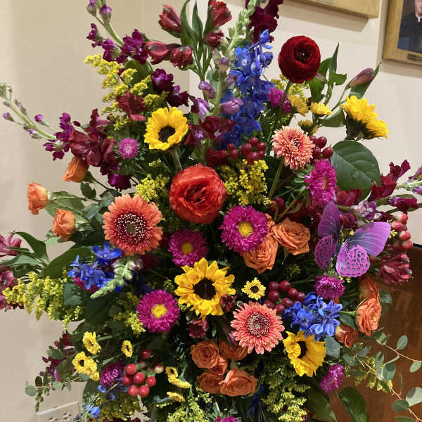 Large colorful standing floral arrangement with sunflowers, roses, and daisies